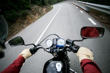 POV view of motorcycle driver driving through mountain road on high speed on vintage retro motorcycle or cafe racer, looks in rear view mirrors and control panel. concept adventure and roadtrip