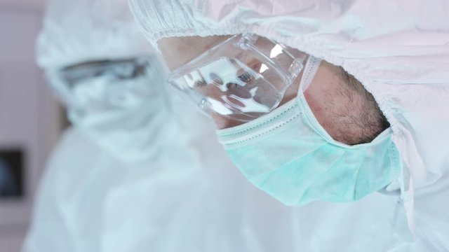 Close up on faces scientific researchers in full body suits working in sterile lab