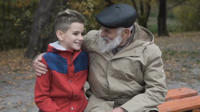 Happy grandfather with grandson at the bench in park