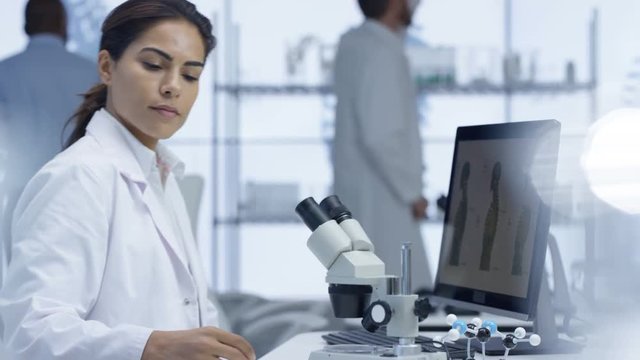  Medical researcher looking at a slide under microscope & working on computer
