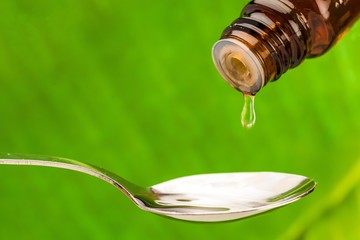 Closeup of a Bottle Pouring Drops on a Spoon with Leaf on