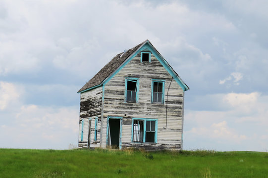 Old abandoned house with white and blue paint in the middle of a field in Saskatchewan, Canada.