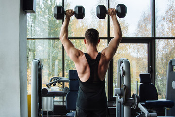 Young handsome man lifts weight in a sporting club. A boy training muscles in a gym. Sportsmen preparing to his future competitions in training center. Best workout for a trainer during work.