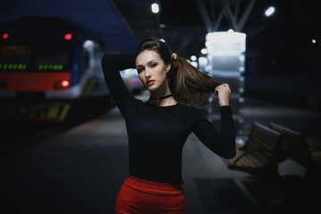 Obraz na płótnie Canvas Beautiful young elegant woman traveler waiting for train at evening train station