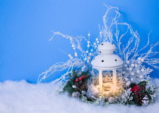 Christmas Eve lantern and decorations background. Picture of a white lantern with lighted candle decorated with pine cones  on a white snow against red frost background
