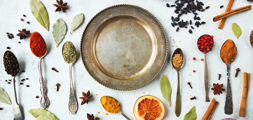 Various colorful indian spices and herbs in silver spoons on white background