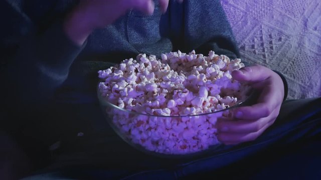 Kid eating popcorn from a bowl while watching a movie on his TV at home