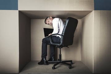 middle-aged businessman in small office working on laptop sits with his back to us