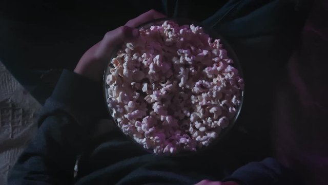 Top view of kid eating popcorn from a bowl while watching TV