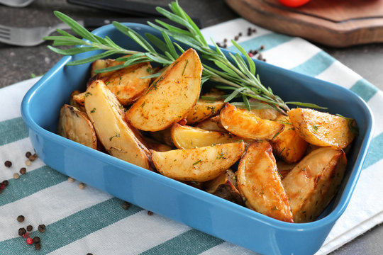 Delicious baked potatoes with rosemary in baking dish on cloth