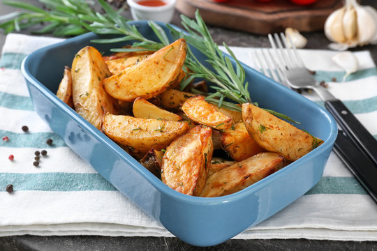 Delicious baked potatoes with rosemary in baking dish on cloth