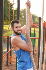 Fototapeta premium Handsome young man doing rope climbing exercise outdoors