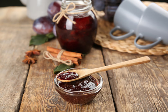Spoon in small bowl with tasty plum jam on wooden table