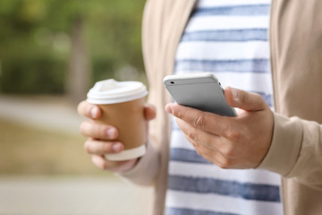 Young man with cup of coffee using his mobile phone outdoors