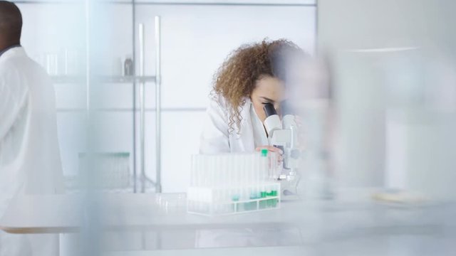  Research scientist working in laboratory, looking at sample under microscope.