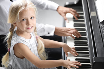 Fototapeta na wymiar Little girl and young man playing piano indoors
