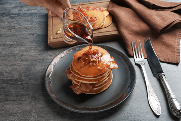 Woman pouring honey onto pancakes with bacon on table