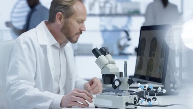  Medical researcher looking at a slide under microscope & working on computer