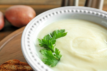 Ceramic bowl with potato cream soup on wooden board