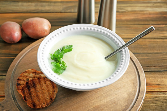 Ceramic bowl with potato cream soup on wooden board