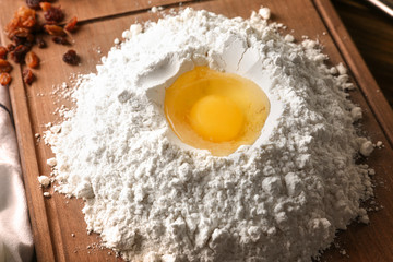 Heap of flour with egg on wooden board, closeup