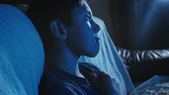 Little boy watching a movie on on TV and eating popcorn