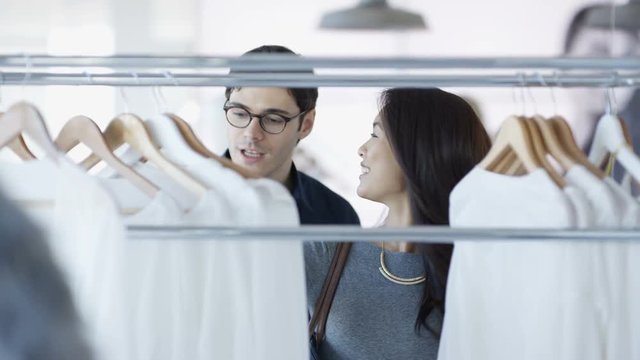 Smiling couple shopping, woman looking at clothes in boutique clothing store.