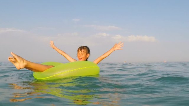 A happy child is spinning on an inflatable circle in the water. A little girl is floating on an inflatable circle in the sea.