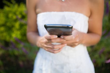 Midsection on bride using mobile phone while standing in yard - Powered by Adobe