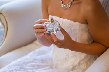 Obraz na płótnie Canvas Midsection of bride holding perfume sprayer while sitting on