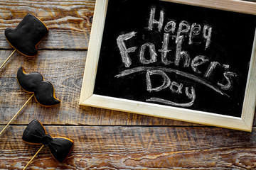 Words happy Father's day written on blackboard. Black tie, mustache and hat cookies. Wooden background top view