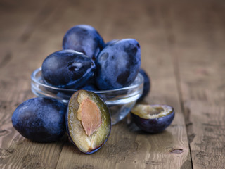 Juicy ripe beautiful plum in a glass bowl on a rustic table.