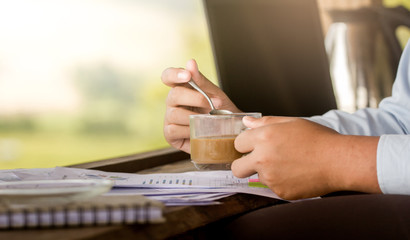 Close-up hands of businessman holding graph documents with coffee cup and working on wooden desk