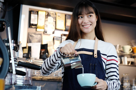 Young asian women barista pouring milk into coffee cup at cafe counter, food and drink concept
