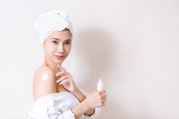 Beautiful girl in bath towel is applying cream on her shoulder.