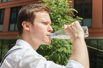 A young office worker is drinking pure water from plastic bottle in hot summer day