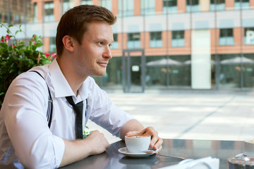 A young businessman is sitting in cafe on outdoor terrace in summer day