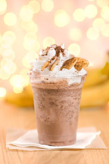 Banana cocoa in a plastic beaker to take out. Chocolate banana smoothie in glass with paper straw on wooden background, selective focus, horizontal, toned