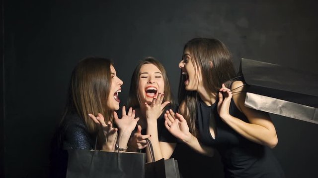 Beautiful caucasian girls, in elegant black clothes, expressing joy with purchases on black friday in the black background