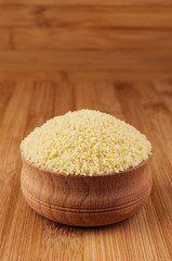 Couscous in wooden bowl on brown bamboo board, closeup.