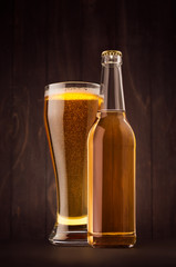 Transparent beer bottle and glass weizen with golden lager on dark brown wood board, vertical, mock up. Template for advertising, design, branding identity.