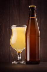 Brown beer bottle NRW and glass tulip with muddy weizen on dark wood board, vertical, mock up. Template for advertising, design, branding identity.