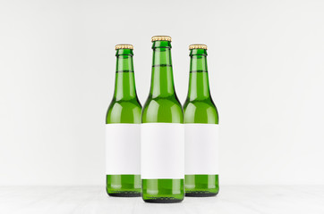 Three green longneck beer bottles 330ml with blank white label on white wooden board, mock up. Template for advertising, design, branding identity.