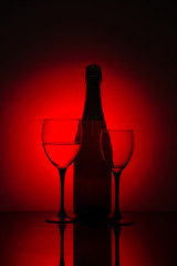 Glasses of champagne and a bottle of wine on a black background with red light