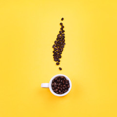 White empty espresso cup with coffee beans in shape of coffee steam, yellow background. Flat lay