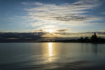 Beautiful sunrise over lake. The rising sun shines through dramatically clouds, silhouette of trees on the shore of lake Balaton, Hungary.