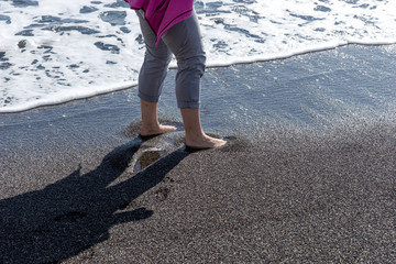 Woman with bare feet in water on the black beach, Santorini Island