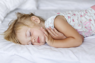 Sweet little blond girl sleeps in bed with her parents.