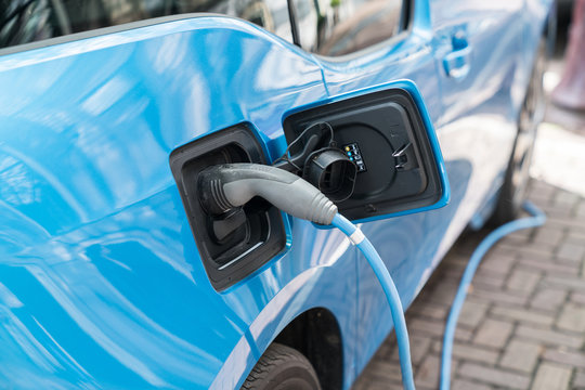 Blue electric car recharging on street with charge cable and plug leading to charge point.