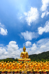 Big golden buddha statue and many small golden buddha statues sitting in row at at Buddha Memorial park, Nakornnayok Thailand.